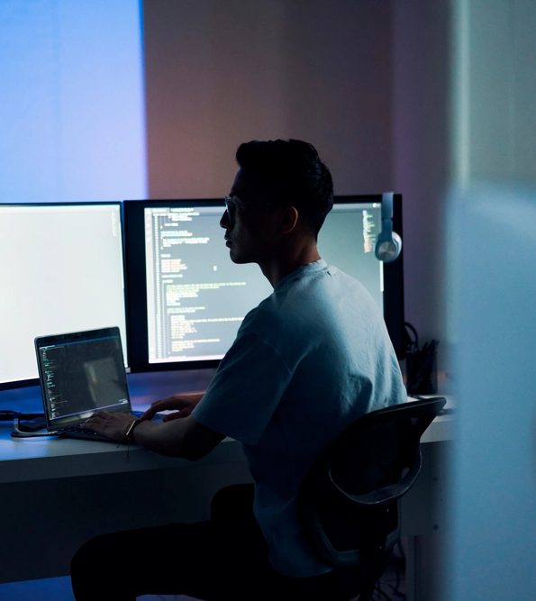 ein Mann, der vor einem Computer und einem Bildschirm sitzt