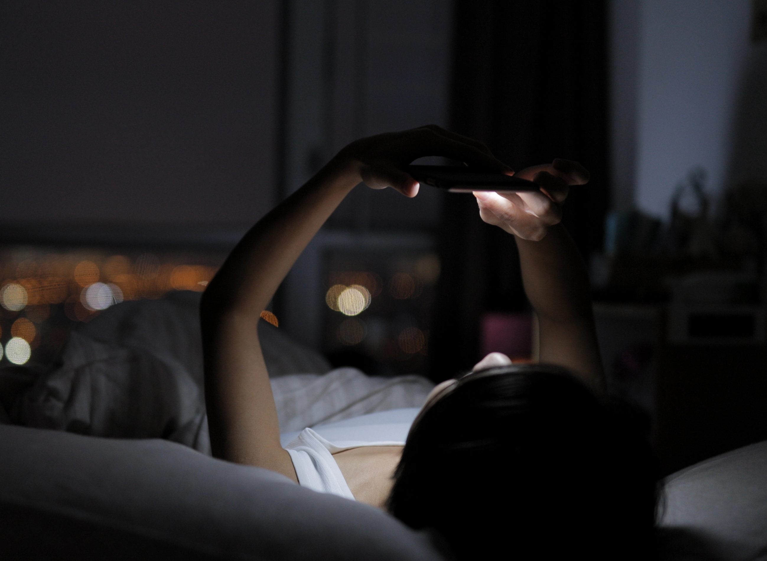 eine Frau, die im Bett liegt und im Dunkeln auf ihr Handy schaut
